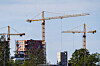 Tre gule heisekraner over en byggeplass i Lillestrøm med bygg under oppføring og trær i forgrunnen.