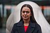 Kamzy Gunaratnam i mørk kåpe og rød topp, fotografert mot en uskarp bybakgrunn i Oslo.